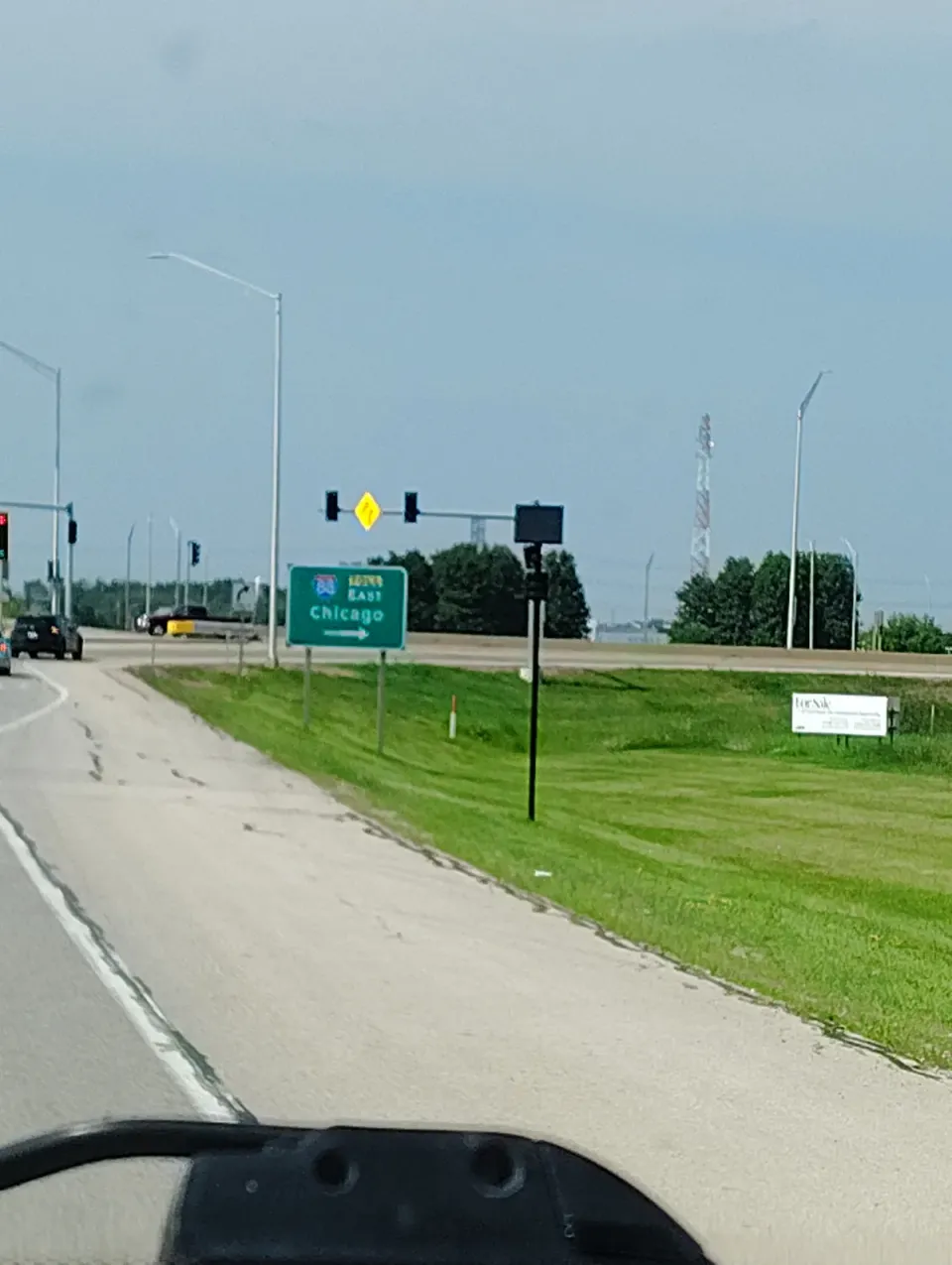View from a car dashboard of a license plate reader mounted on a pole at a highway interchange, beside a sign reading Interstate 88 East to Chicago