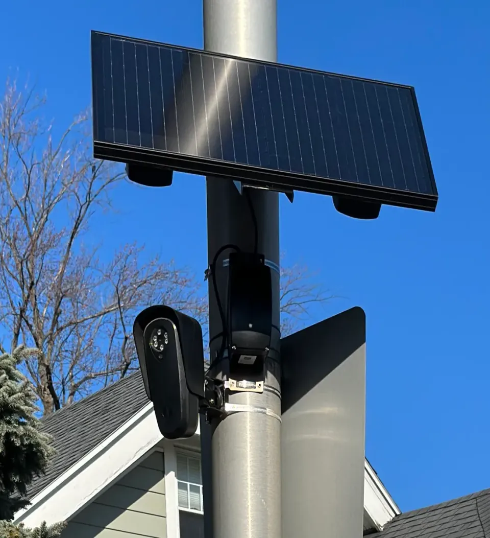 A license plate reader camera and solar panel mounted on a pole directly in front of a residential house